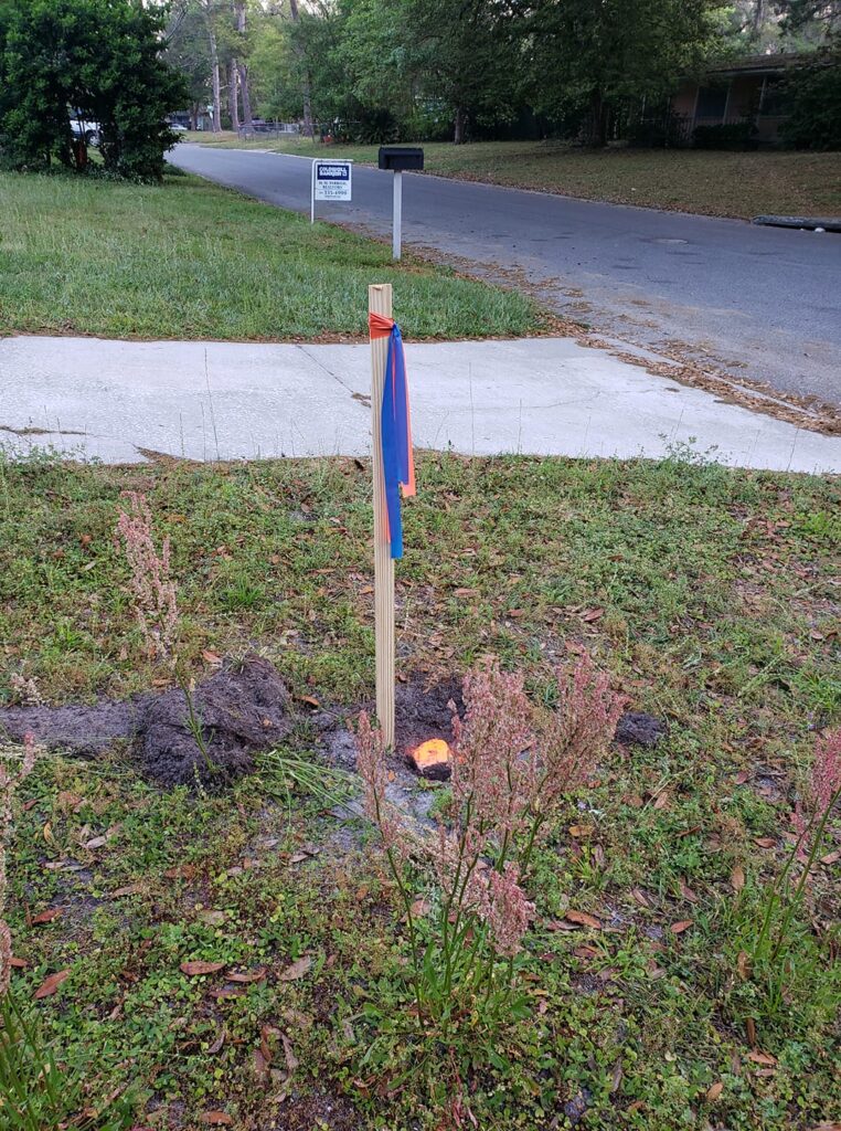 a wooden stake with colored tips is in the ground in a front yard