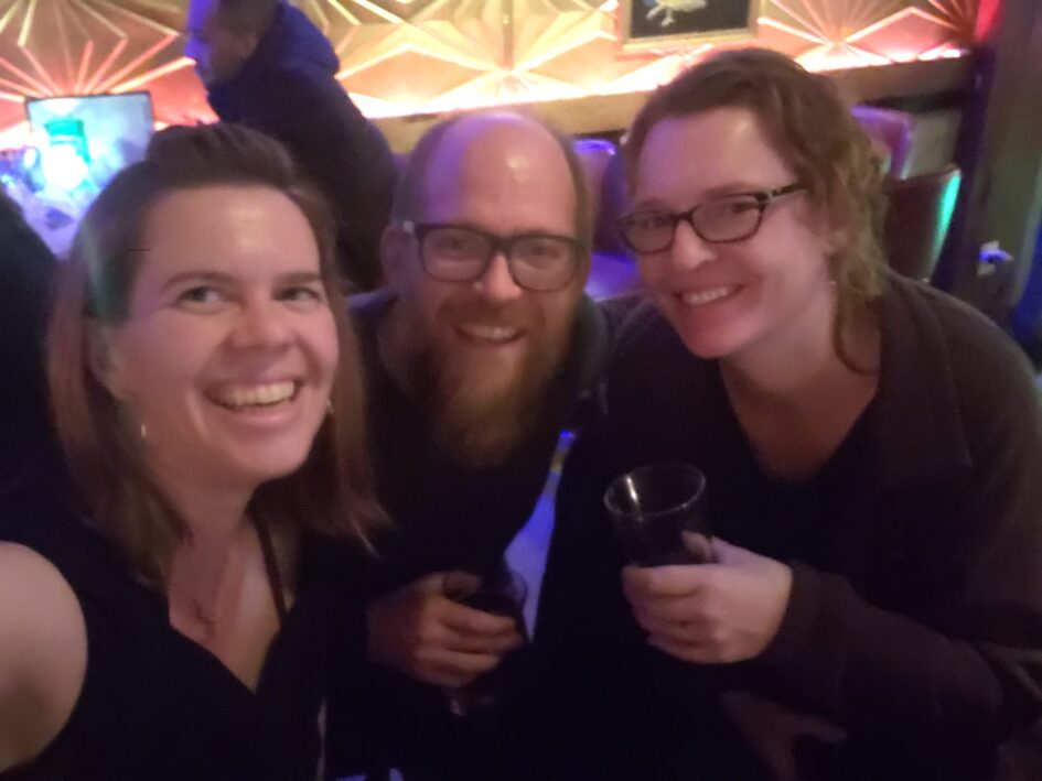 a blurry selfie of three people in some kind of dark bar holding glasses