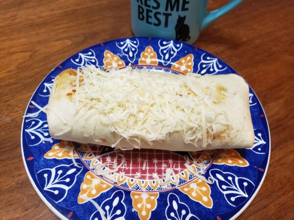 a burrito covered in cheese is sitting on a colorful plate
