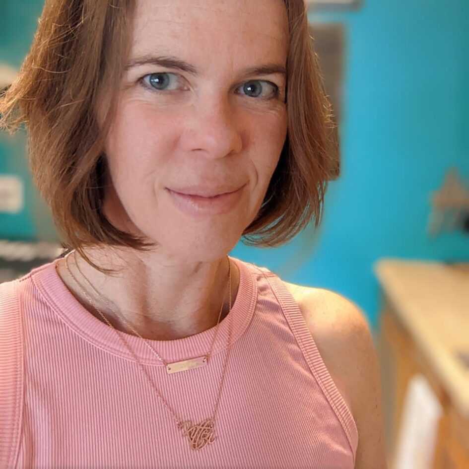 selfie of a woman in a pink dress with a vibrant teal green wall behind her
