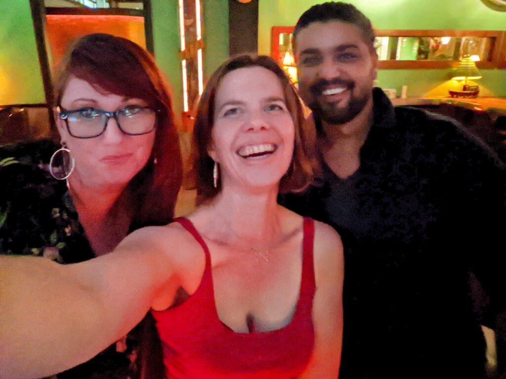a selfie of three people with a colorful club or restaurant in the background