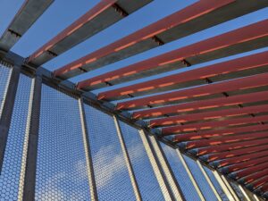 some kind of large metal structure with regular red beams running down one side like ribs and mesh and beams running down the other side