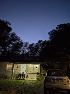the lighted front porch of a home and car in the driveway under a deeply blue night sky