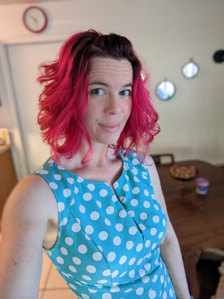 a selfie of a person with dark unnaturally red colored hair wearing a bright seafoam green dress with large polka dots