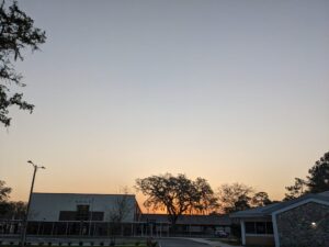 a clear sky is faded from steel gray down to soft pink as it dips behind a low square building that looks like a school