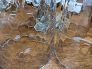 close up of two glasses with square textures that distort the light and show the wood table underneath