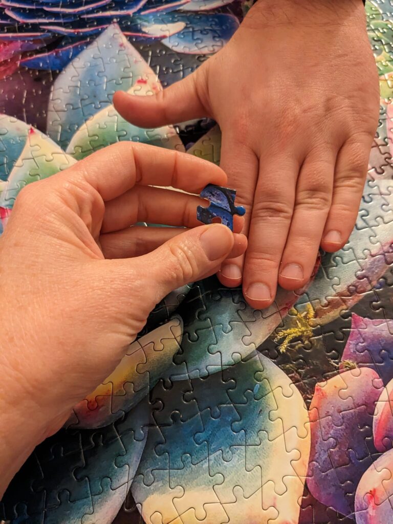 two hands on a complete puzzle with one holding a puzzle piece