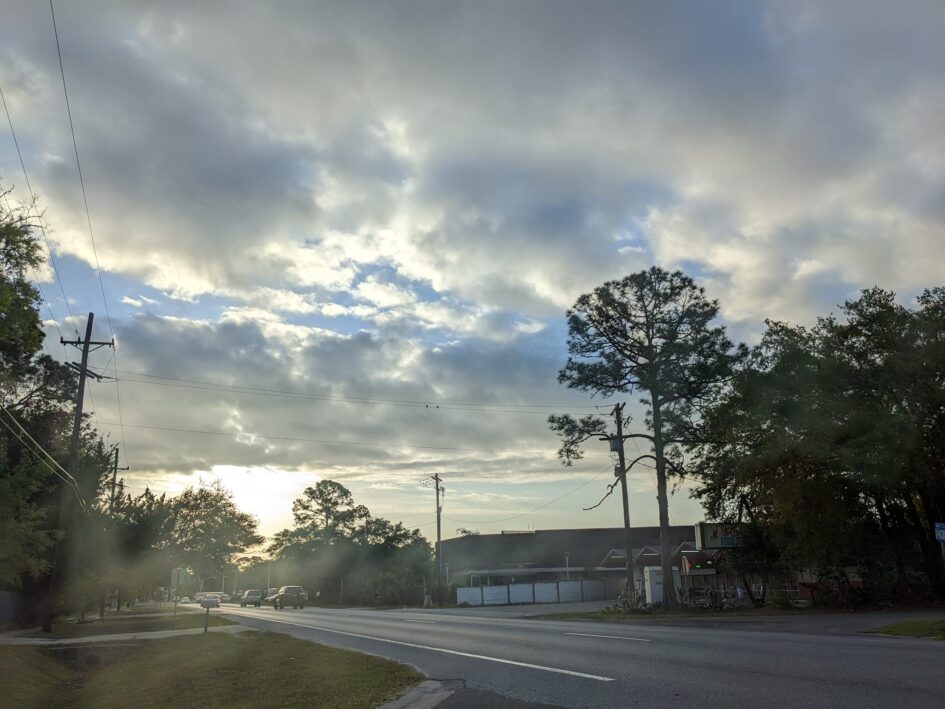 a street scene with large building on one side ad clouds overhead catching sunlight