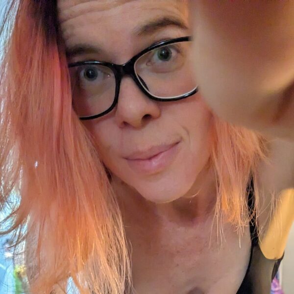 close up selfie of a person in black framed glasses and pale golden pink hair