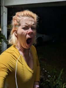 a selfie of a person yawning with a dark yard behind them