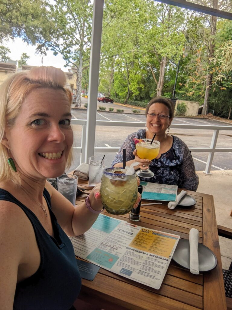 selfie of two people at a restaurant patio table holding large cocktail glasses