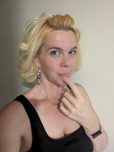 selfie of a blond person in a black dress making a face
