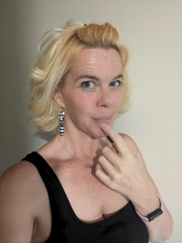 selfie of a blond person in a black dress making a face