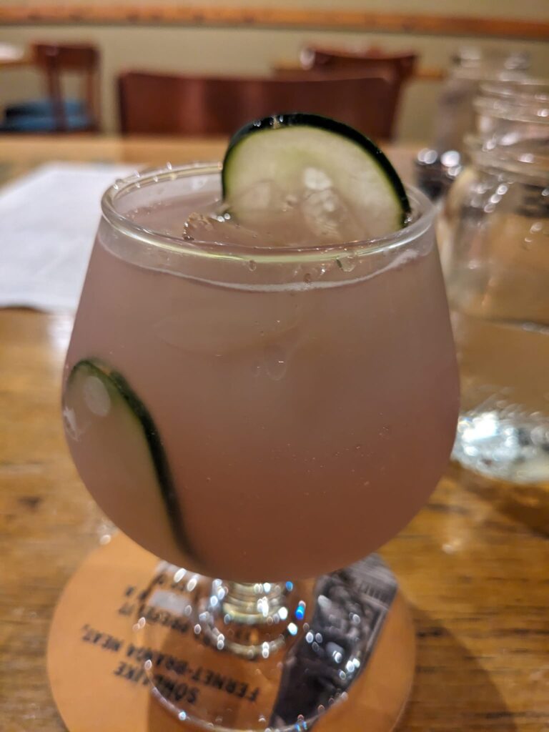 a pink cocktail with a long slice of cucumber in it