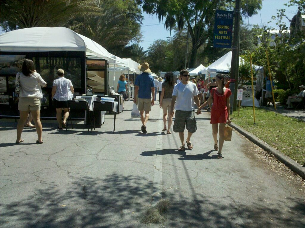 a small crowd of people are walking on a street between booths at an art fair