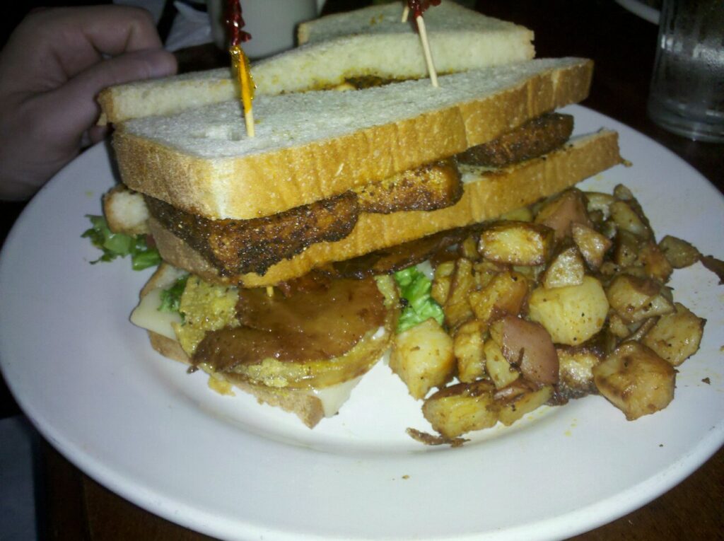 a tall sandwich on a plate with cubed potatoes