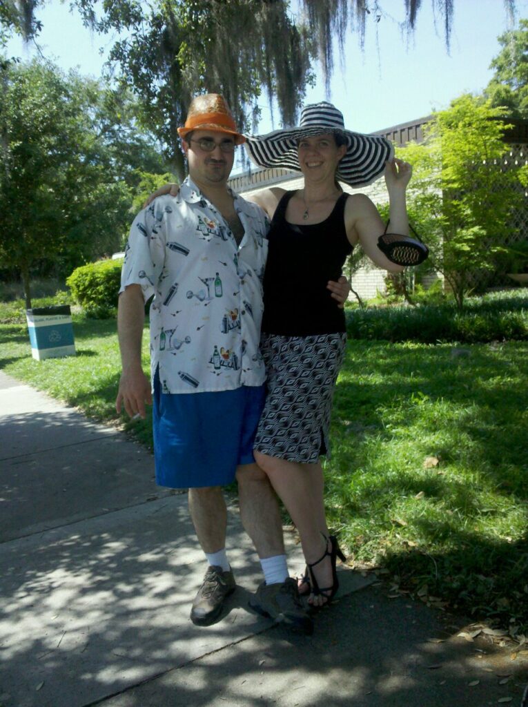 two people in unusual hats are posing for a portrait along a grassy sidewalk