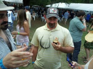 several people are holding glasses of beer with a crowd and tents behind them in a park