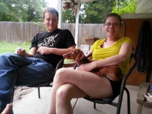 two people are sitting on a porch and one is holding a small dog