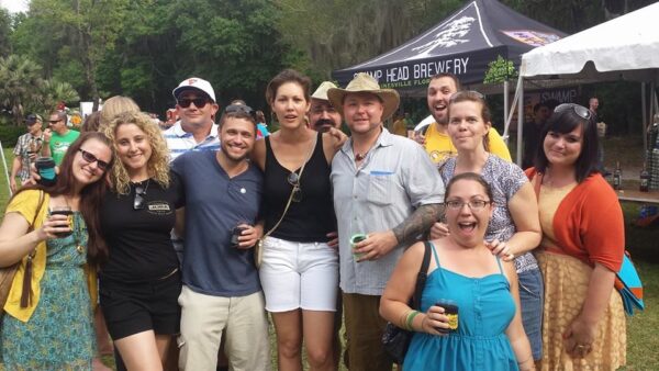 a large group of people are standing for a photo outside with a brewery tent behind them