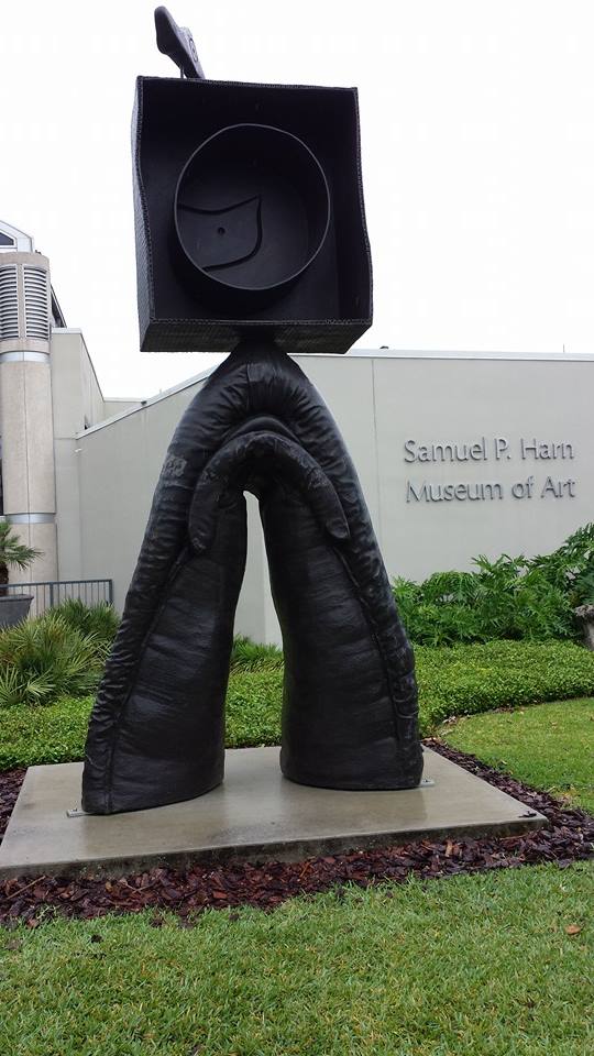 a large art sculpture outside a museum that looks like a box on top of an organic looking arch made of dark metal