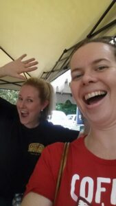 selfie of one person with another person making a face and jazz hands behind her