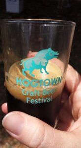 a hand is holding a small glass half full with a boar logo and the words Hogtown craft beer festival