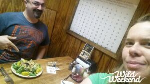 selfie of two people at a restaurant table and one is pointing at a salad