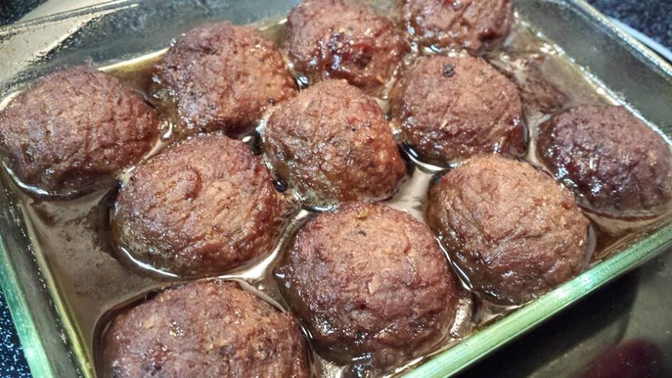 a dozen meatballs are baked dark in a shallow dish of oil