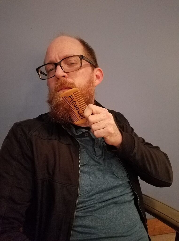 a mad is combing his long red beard with a comb with the lettering Fight Me!