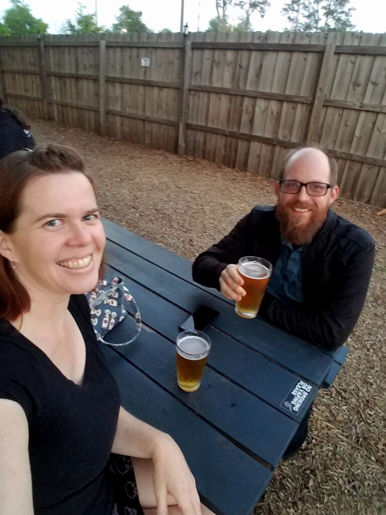 two people are sitting at a picknick table with pints of beer