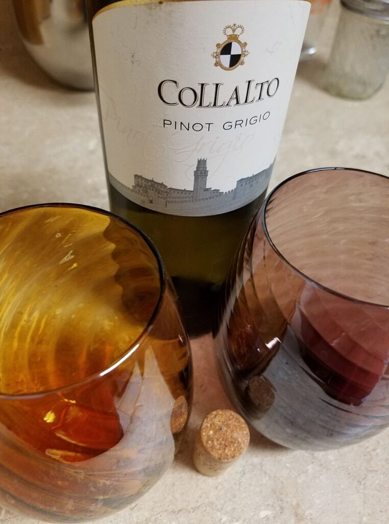 a bottle of wine is flanked by two colorful glasses