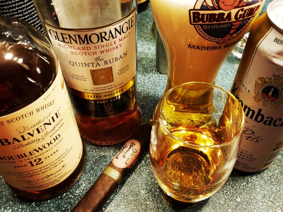 several whiskey bottles and a glass of whiskey surround a cigar