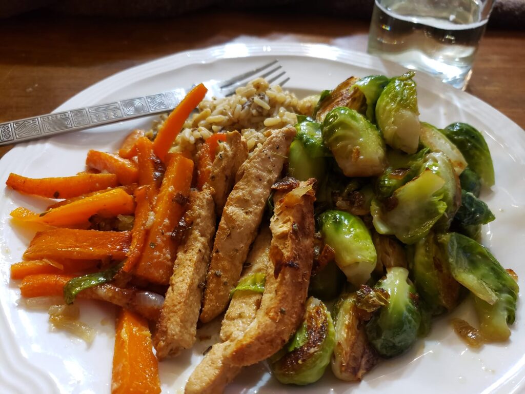 a dinner plate has brussel sprouts, carrots and chicken strips