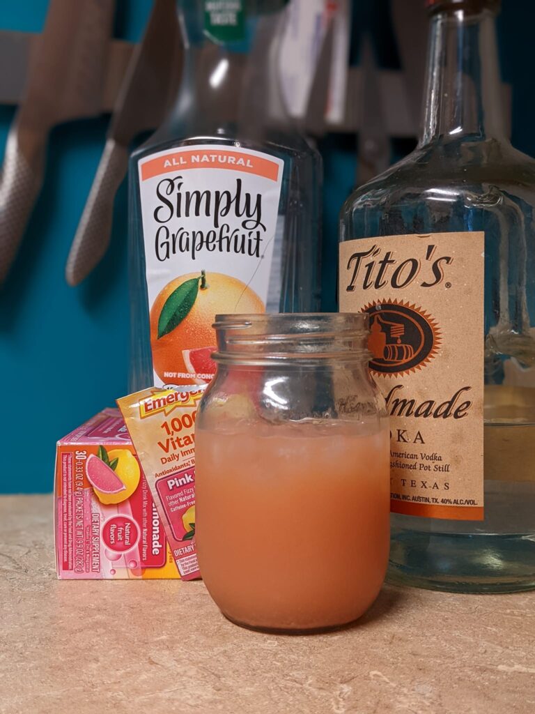 a glass of grapefruit juice next to a bottle of vodka, a bottle of grapefruit juice and a box of Emergen-C
