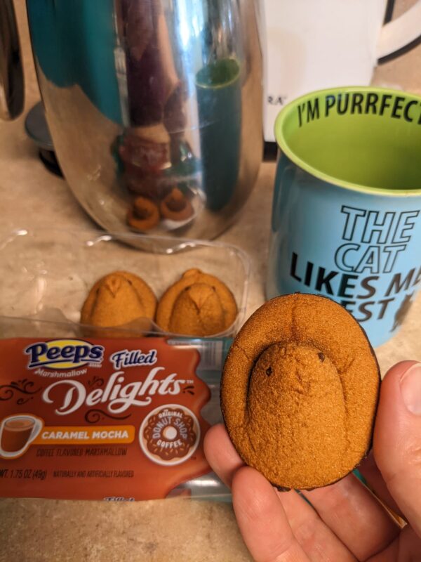 a hand holds a brown Peep in front of a coffee cup