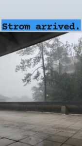 a cement patio with a roof overhang looking out over a heavy rainfall with some pine trees blurry in the foreground