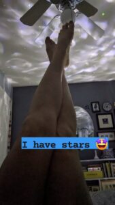 legs are held up towards a ceiling fan and there is blobby galaxy lighting being projected on the ceiling