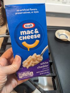 a hand holding a box of Kraft mac and cheese