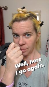 selfie of a person with yellow hair gathered up in several knots and text saying Well, here I go again