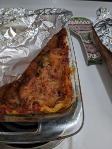 aluminum foil is peeled back from a baked dish like a lasagna