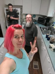 selfie of a person with two people in the kitchen behind her