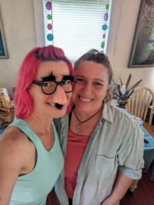selfie of two people in a dining room with one wearing a fake nose and glasses