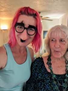 selfie of two people in a dining room with one wearing a fake nose and glasses
