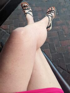 a view downward at a pair of crossed legs with a short skirt and strappy shoes