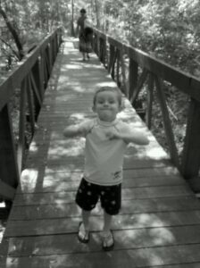a small child is making a face on a wooden walkway through a forest