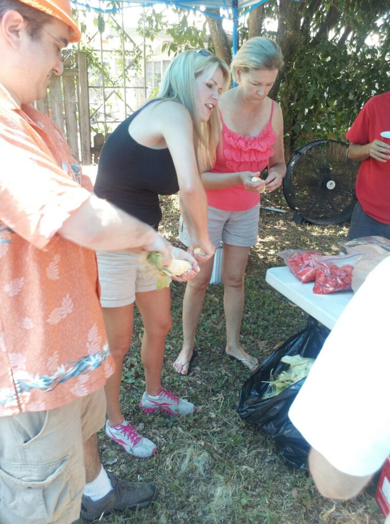 several people are standing around a table outside possibly shucking corn