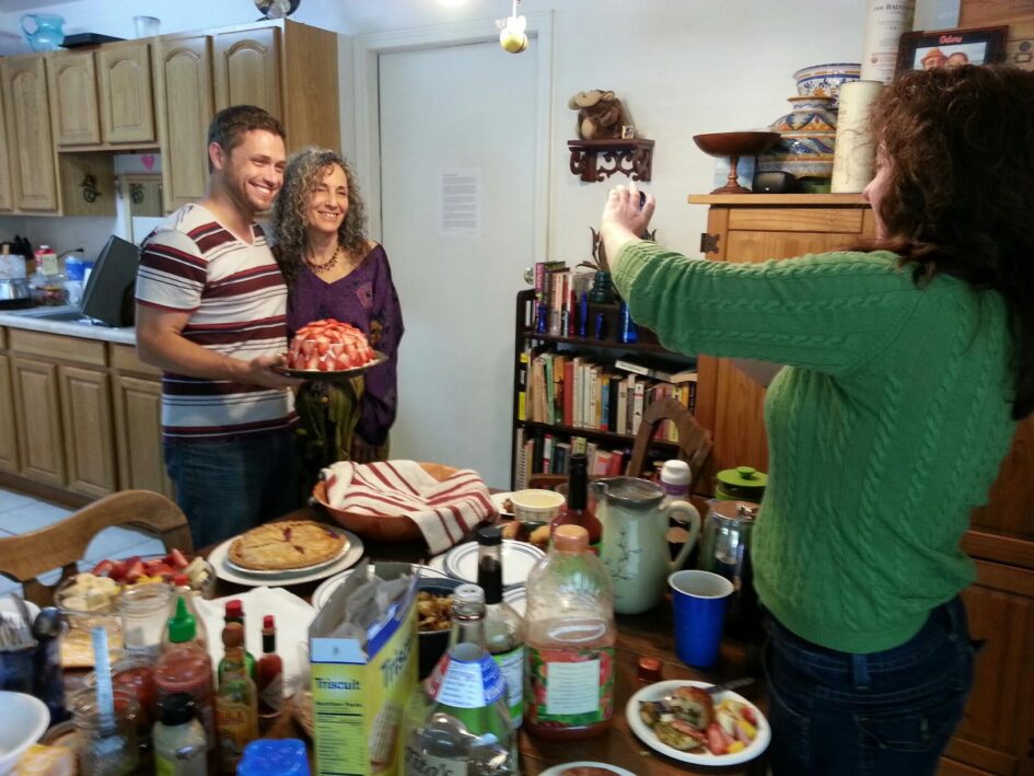 someone on one side of a crowded table is taking a picture of two people on the other side of all of the food