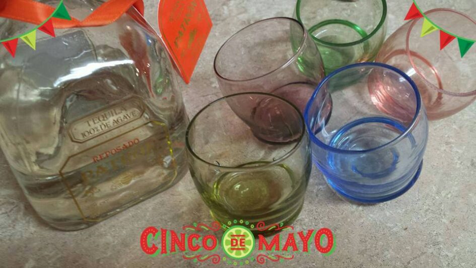 a set of multi colored rounded shot glasses next to a bottle of Patron tequila