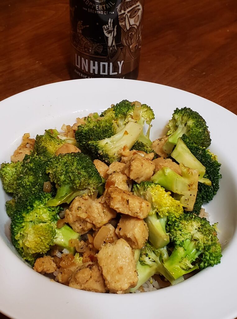 a plate of food includes broccoli and rice and a beer next to it